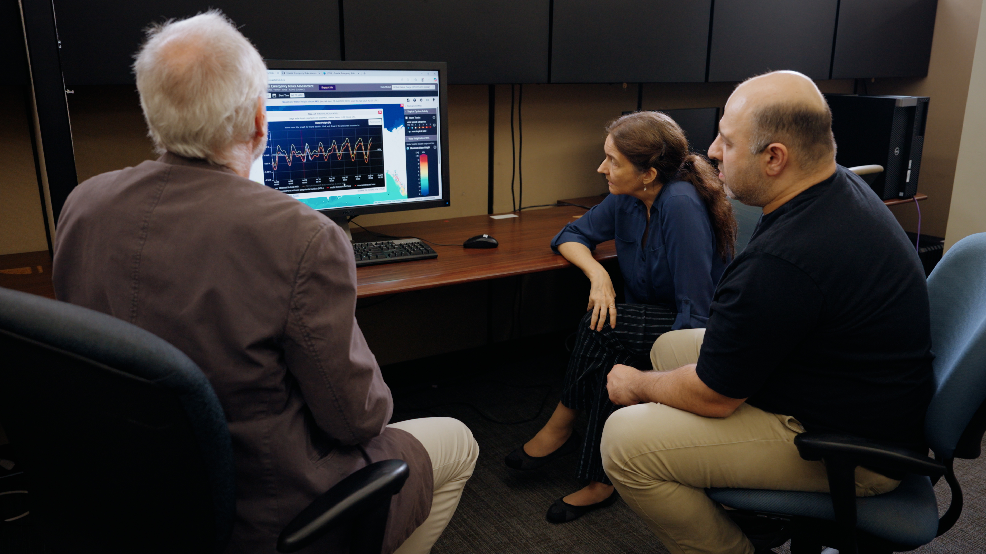 Three  researchers gathered around a computer screen displaying the CERA storm surge tool