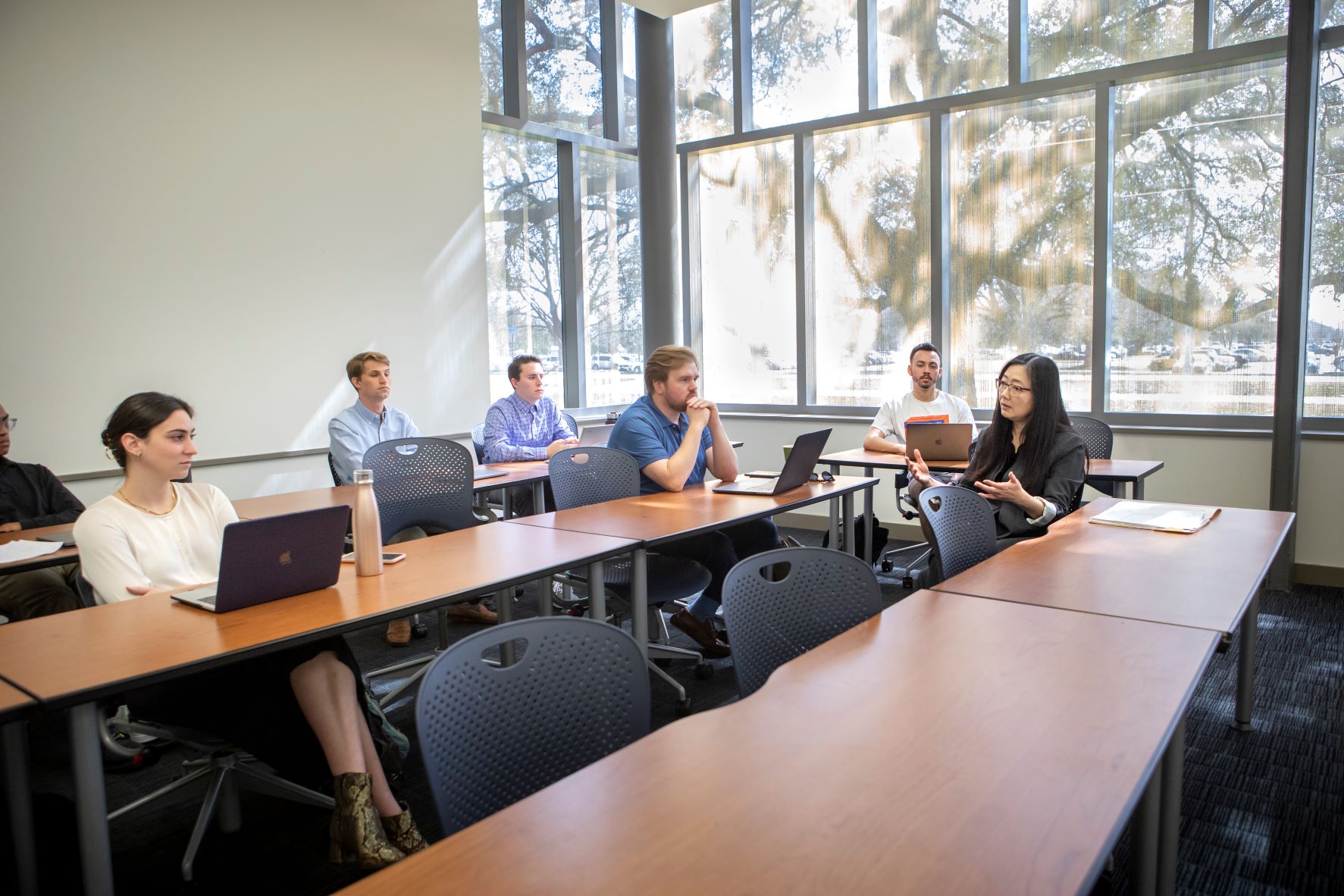 people sit at long desks to talk. it's in front of a window and light is streaming in. 