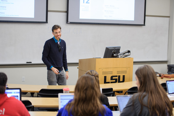 Professor smiles in front of classroom next to a podium.