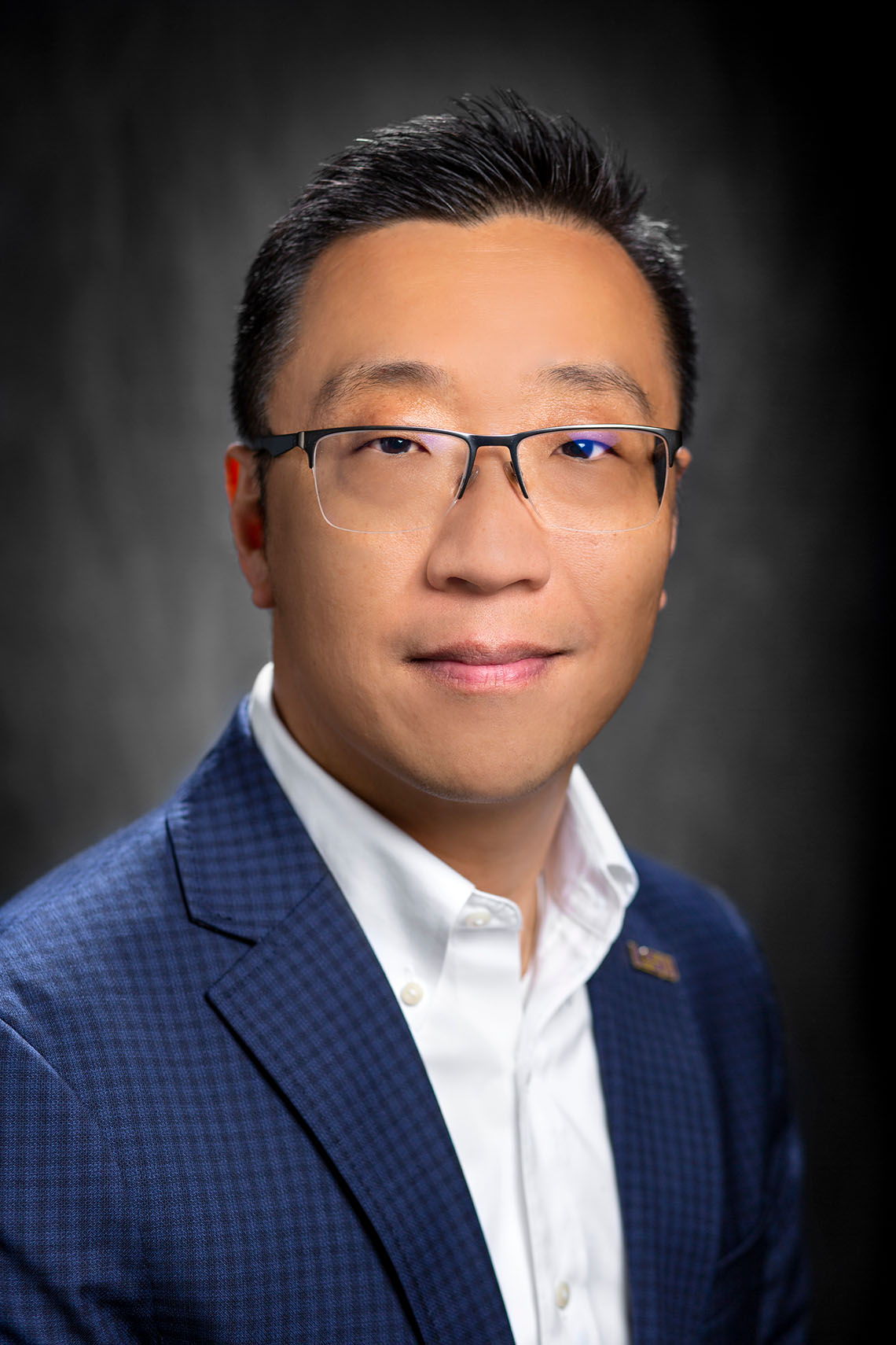 A man wears a blazer and smiles at the camera