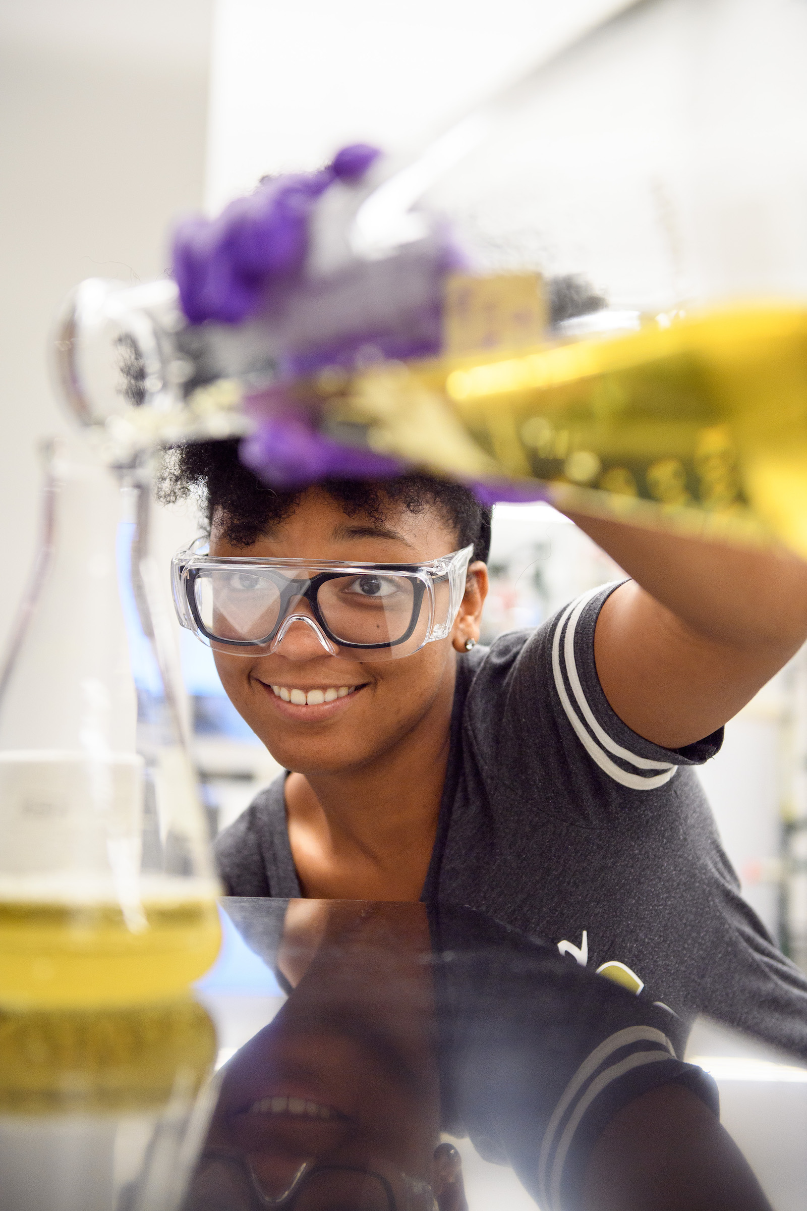 Student pours yellow liquid into beaker.