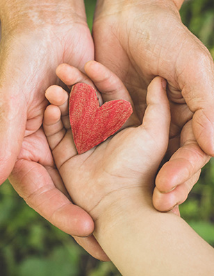 Photo of two sets of hands holding a wooden red heart